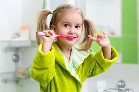 Smiling kid child girl brushing teeth in bathroom