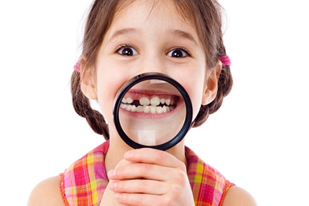 Funny girl showing teeth through a magnifying glass, isolated on white