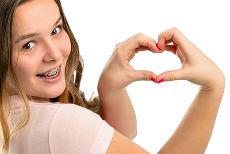 Beautiful happy teenage girl shows gesture heart on a white background.